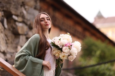 Photo of Charming woman with bouquet of beautiful peonies on city street. Space for text