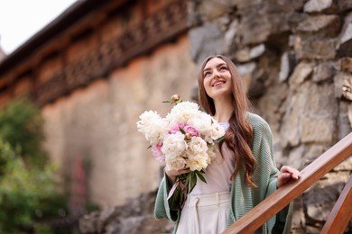 Photo of Charming woman with bouquet of beautiful peonies on city street. Space for text