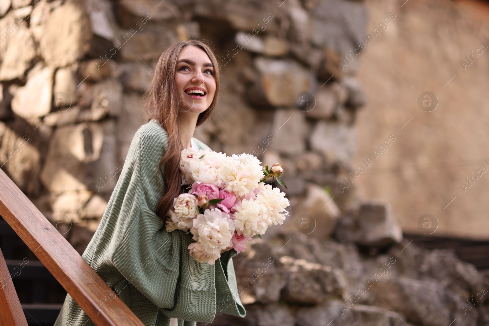Charming woman with bouquet of beautiful peonies on city street. Space for text Photo of Charming woman with bouquet of beautiful peonies on city street. Space for text