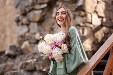 Photo of Charming woman with bouquet of beautiful peonies on city street. Space for text