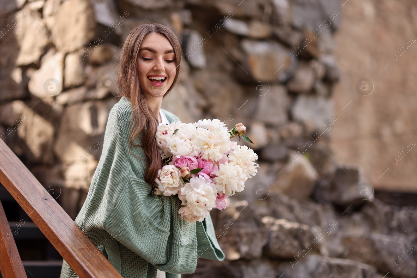 Charming woman with bouquet of beautiful peonies on city street. Space for text Photo of Charming woman with bouquet of beautiful peonies on city street. Space for text
