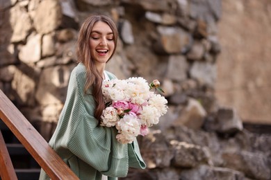 Photo of Charming woman with bouquet of beautiful peonies on city street. Space for text