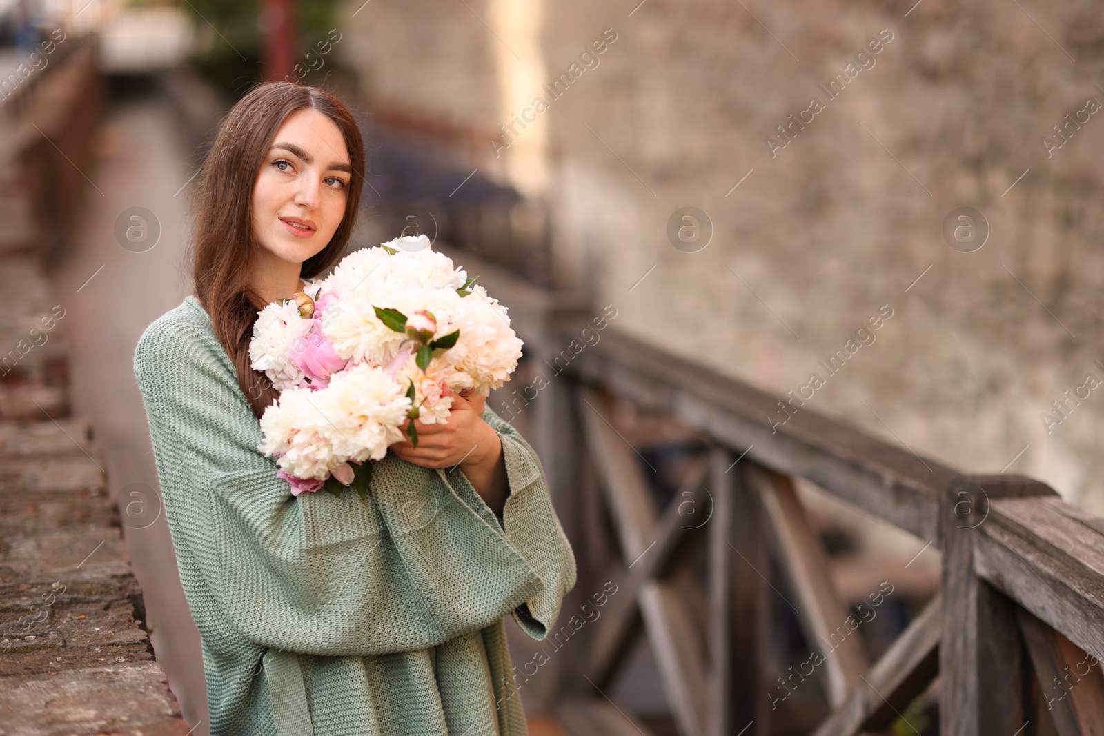Charming woman with bouquet of beautiful peonies on city street. Space for text Photo of Charming woman with bouquet of beautiful peonies on city street. Space for text