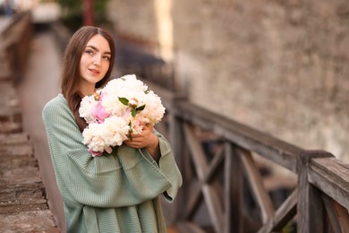 Photo of Charming woman with bouquet of beautiful peonies on city street. Space for text