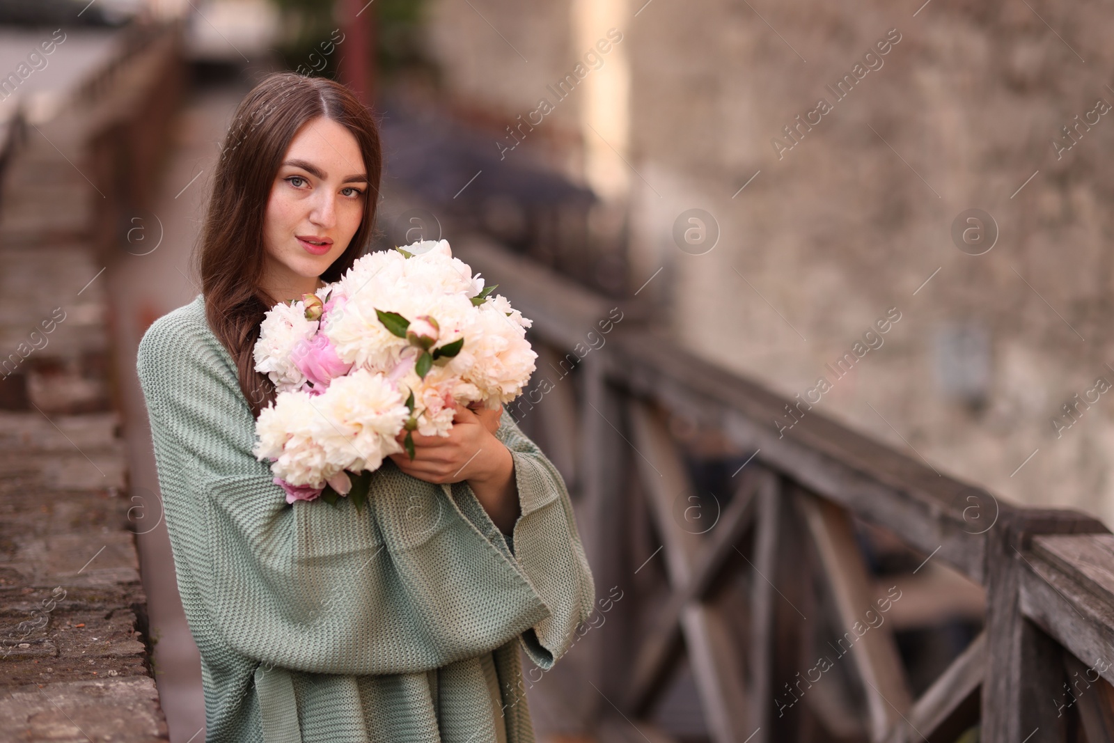 Charming woman with bouquet of beautiful peonies on city street. Space for text Photo of Charming woman with bouquet of beautiful peonies on city street. Space for text