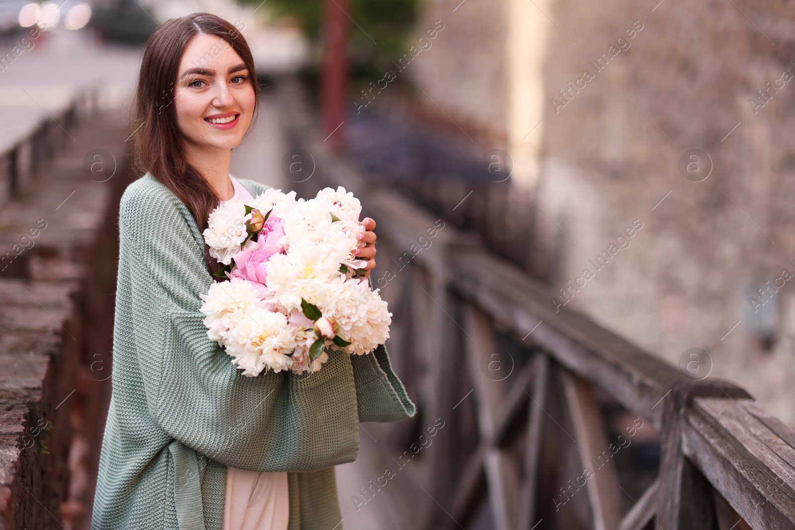 Charming woman with bouquet of beautiful peonies on city street. Space for text Photo of Charming woman with bouquet of beautiful peonies on city street. Space for text