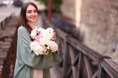 Photo of Charming woman with bouquet of beautiful peonies on city street. Space for text