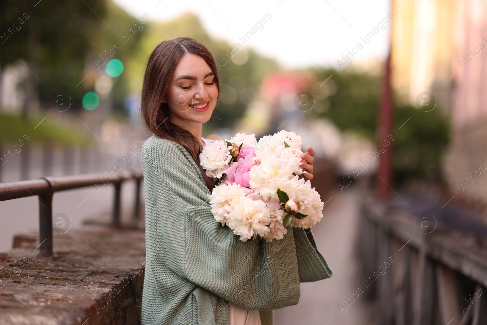 Charming woman with bouquet of beautiful peonies on city street. Space for text Photo of Charming woman with bouquet of beautiful peonies on city street. Space for text