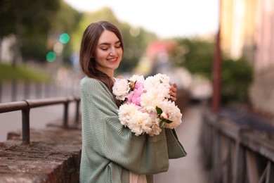 Photo of Charming woman with bouquet of beautiful peonies on city street. Space for text