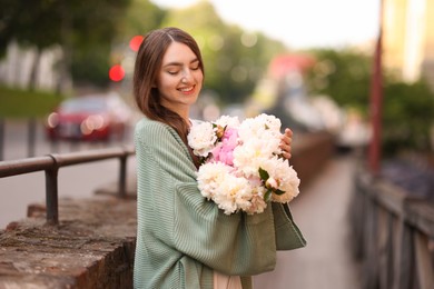 Photo of Charming woman with bouquet of beautiful peonies on city street. Space for text