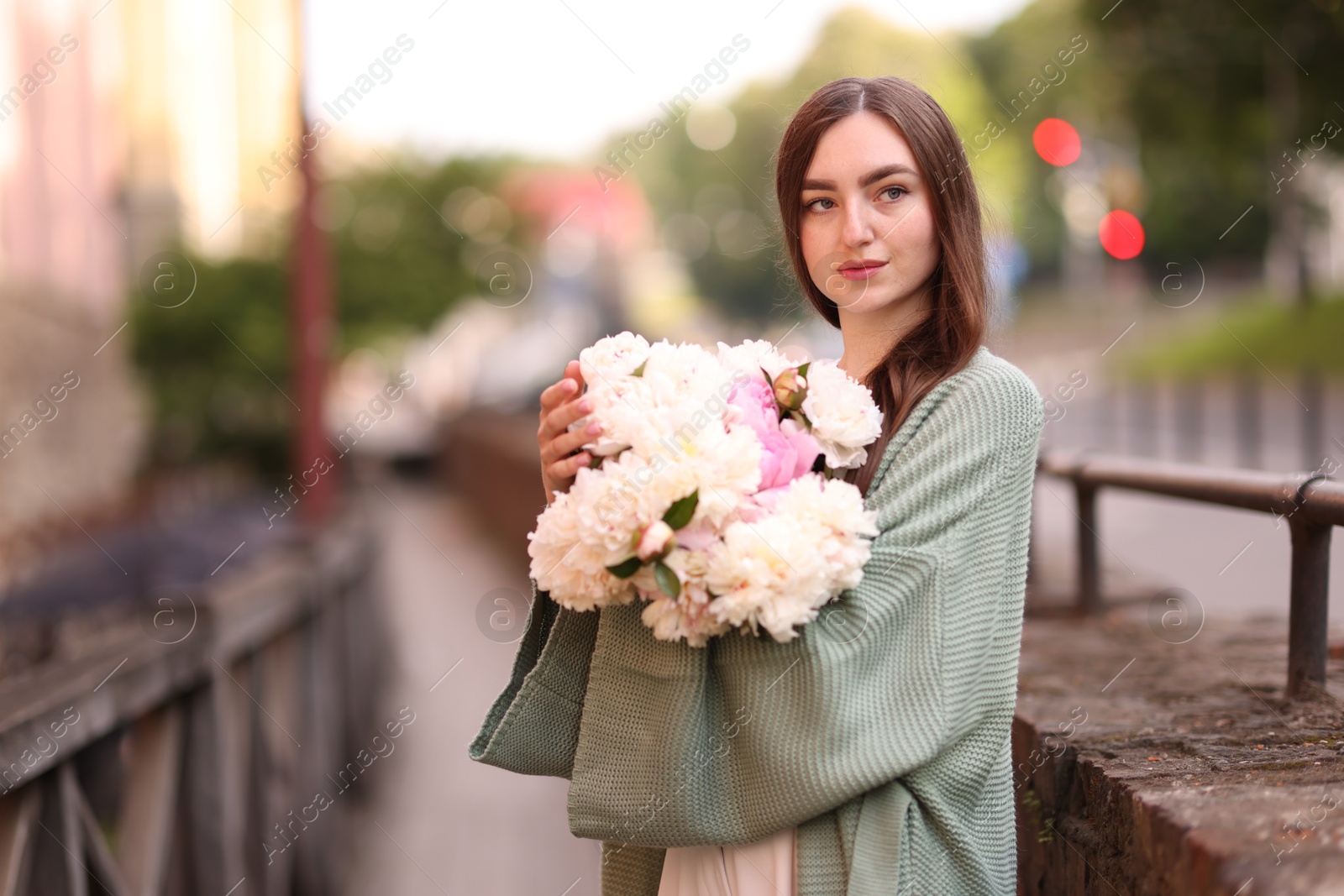 Charming woman with bouquet of beautiful peonies on city street. Space for text Photo of Charming woman with bouquet of beautiful peonies on city street. Space for text