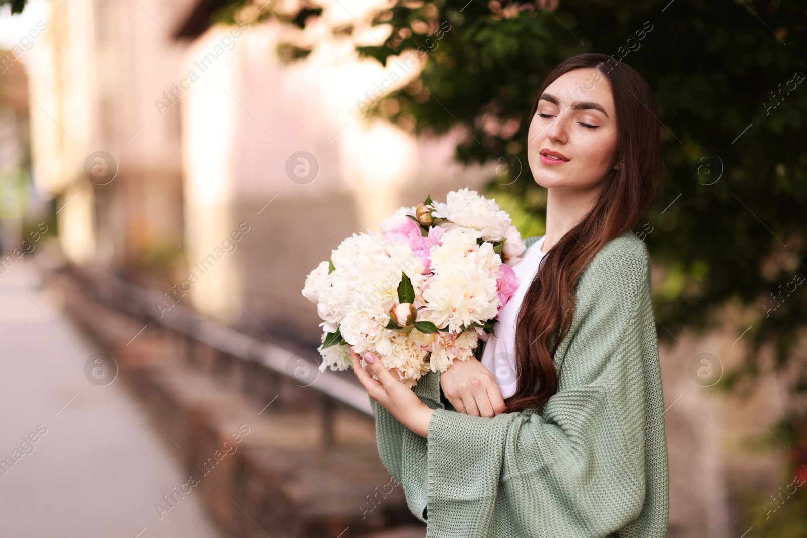 Photo of Charming woman with bouquet of beautiful peonies on city street. Space for text