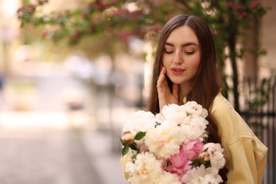 Photo of Woman with bouquet of beautiful peonies on city street. Space for text