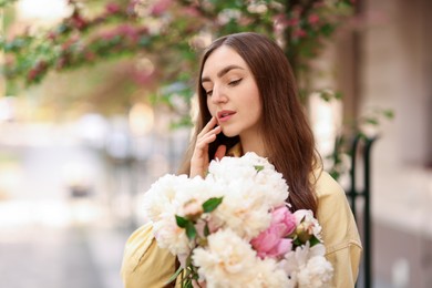 Photo of Woman with bouquet of beautiful peonies on city street. Space for text