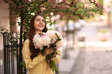Photo of Woman with bouquet of beautiful peonies on city street. Space for text
