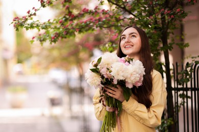 Photo of Woman with bouquet of beautiful peonies on city street. Space for text