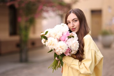 Photo of Woman with bouquet of beautiful peonies on city street. Space for text