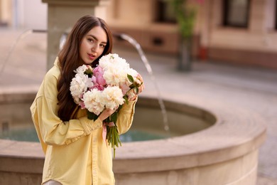 Photo of Woman with bouquet of beautiful peonies on city street. Space for text