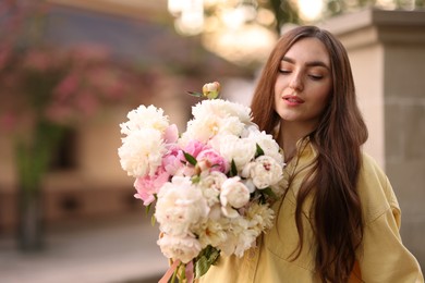 Photo of Woman with bouquet of beautiful peonies on city street. Space for text