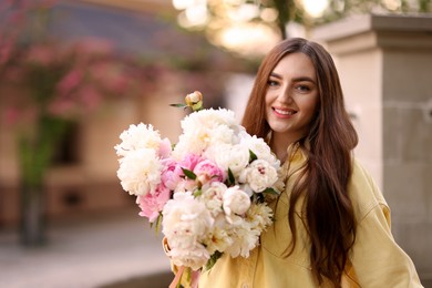 Photo of Woman with bouquet of beautiful peonies on city street. Space for text