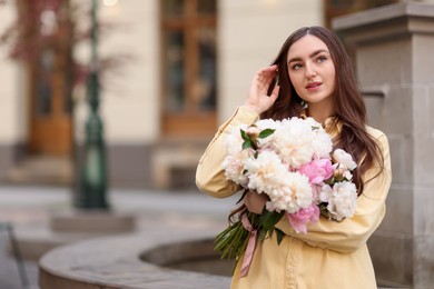 Photo of Woman with bouquet of beautiful peonies on city street. Space for text