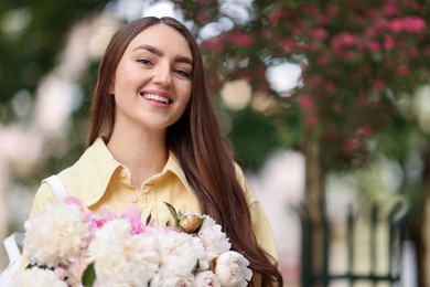 Photo of Woman with bouquet of beautiful peonies on city street. Space for text