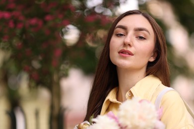 Photo of Woman with bouquet of beautiful peonies on city street. Space for text