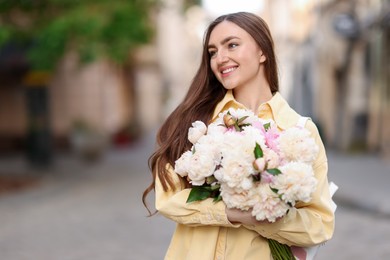 Photo of Woman with bouquet of beautiful peonies on city street. Space for text