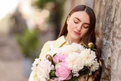 Photo of Woman with bouquet of beautiful peonies on city street. Space for text