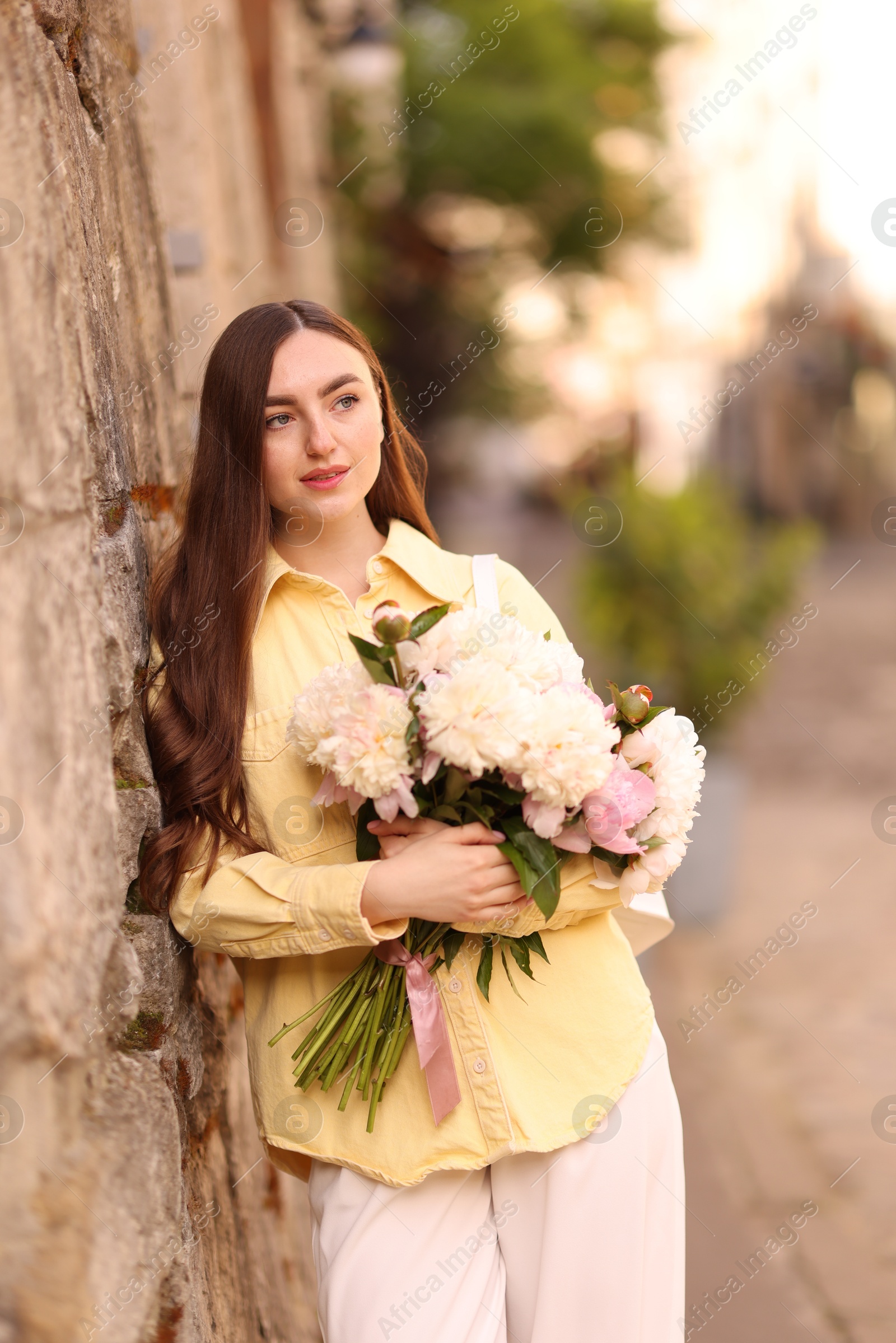 Woman with bouquet of beautiful peonies on city street Photo of Woman with bouquet of beautiful peonies on city street