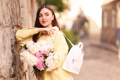 Photo of Woman with bouquet of beautiful peonies on city street. Space for text