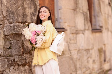 Photo of Woman with bouquet of beautiful peonies on city street. Space for text
