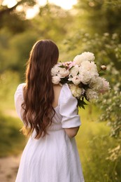 Photo of Beautiful woman with bouquet of peonies in park, back view
