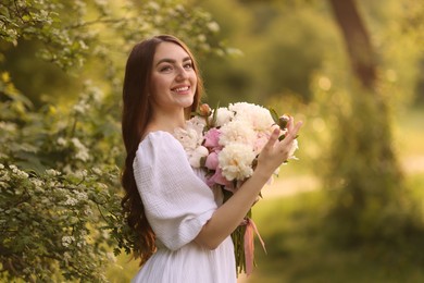 Photo of Beautiful woman with bouquet of peonies in park