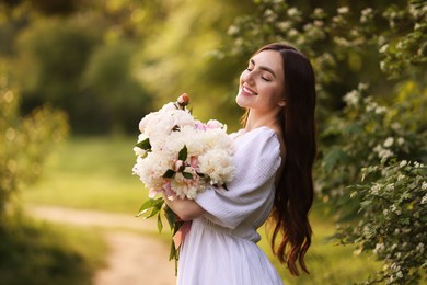 Photo of Beautiful woman with bouquet of peonies in park. Space for text