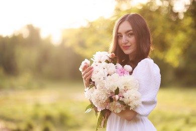 Photo of Beautiful woman with bouquet of peonies in park on sunny day. Space for text