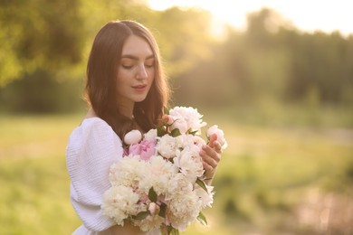 Photo of Beautiful woman with bouquet of peonies in park on sunny day. Space for text