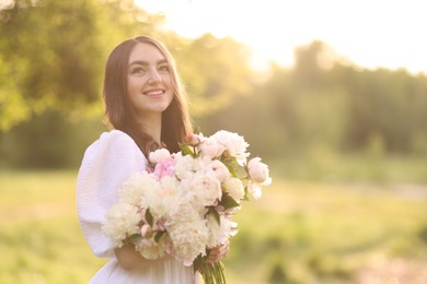 Photo of Beautiful woman with bouquet of peonies in park on sunny day. Space for text
