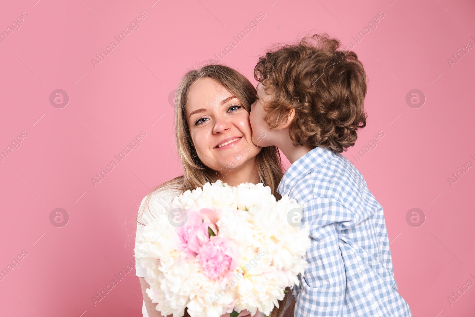 Little boy kissing his mom and giving her beautiful peony flowers on pink background Photo of Little boy kissing his mom and giving her beautiful peony flowers on pink background