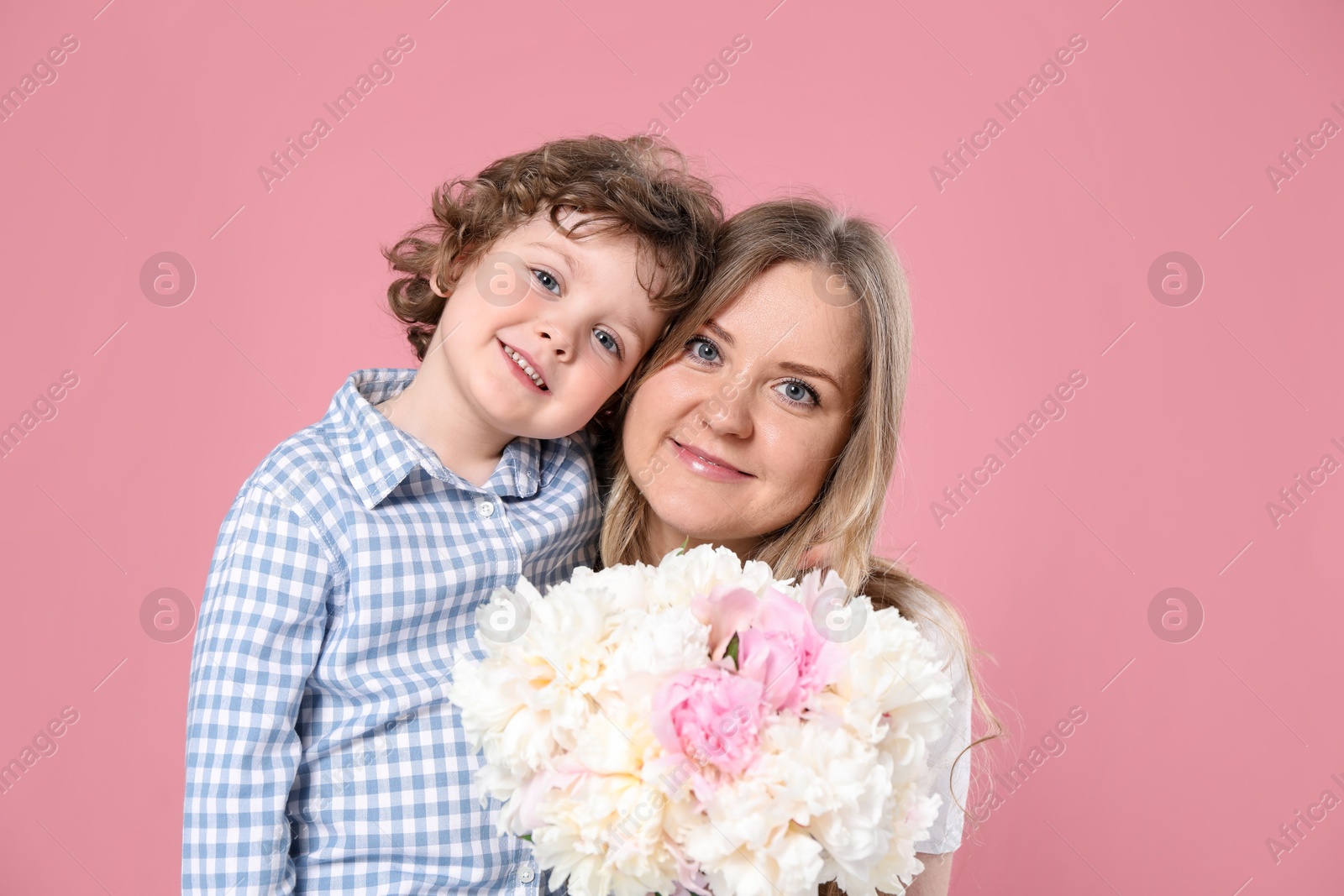 Little boy giving his mom beautiful peony flowers on pink background Photo of Little boy giving his mom beautiful peony flowers on pink background