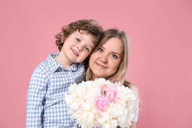 Photo of Little boy giving his mom beautiful peony flowers on pink background