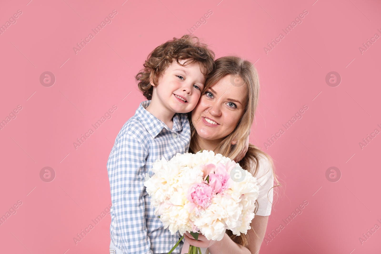 Little boy giving his mom beautiful peony flowers on pink background Photo of Little boy giving his mom beautiful peony flowers on pink background
