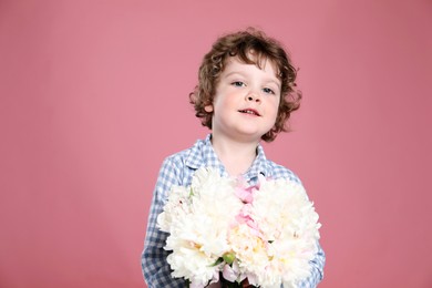 Photo of Cute little boy with bouquet of beautiful peonies on pink background. Space for text