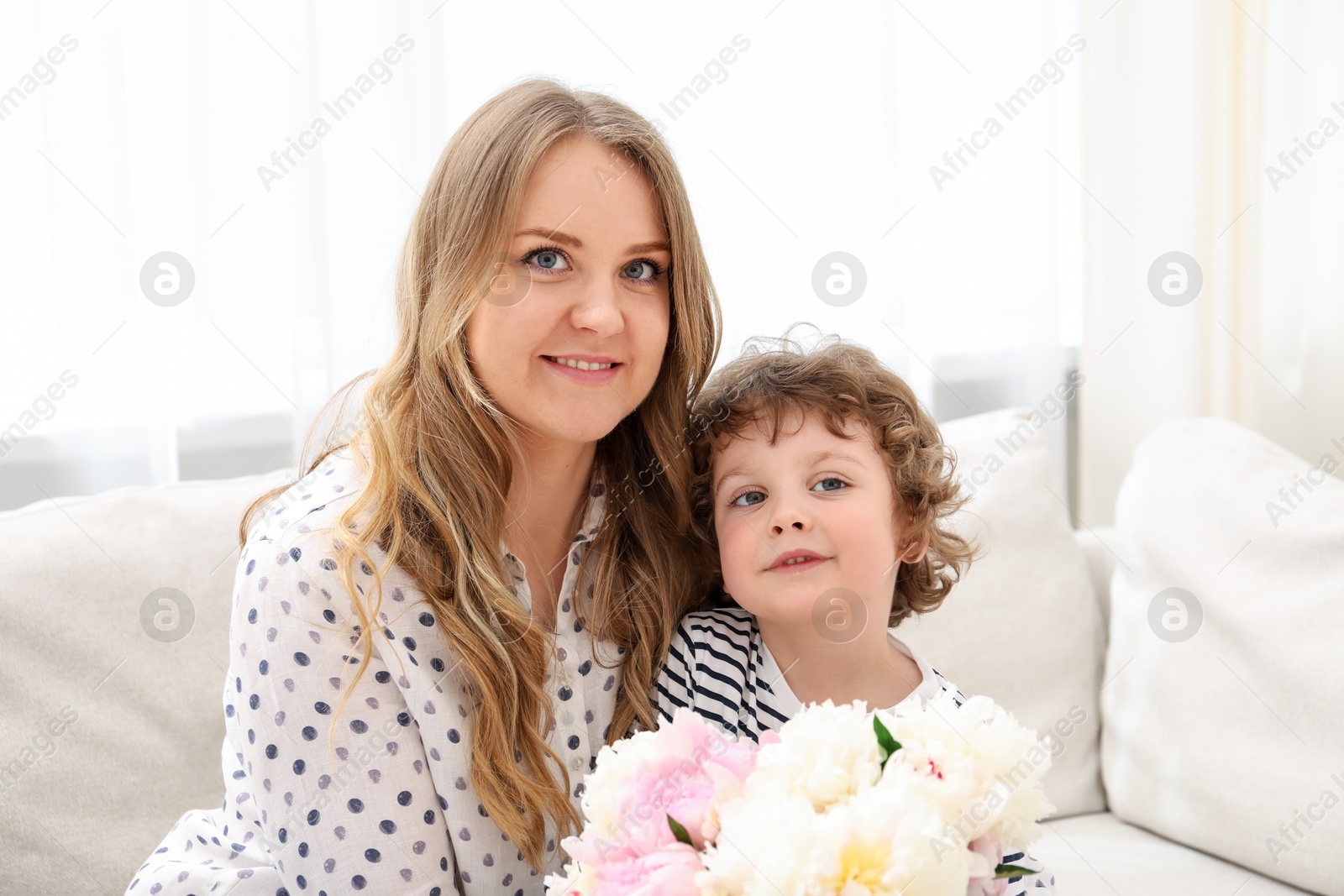 Little boy giving his mom beautiful peony flowers on sofa at home Photo of Little boy giving his mom beautiful peony flowers on sofa at home