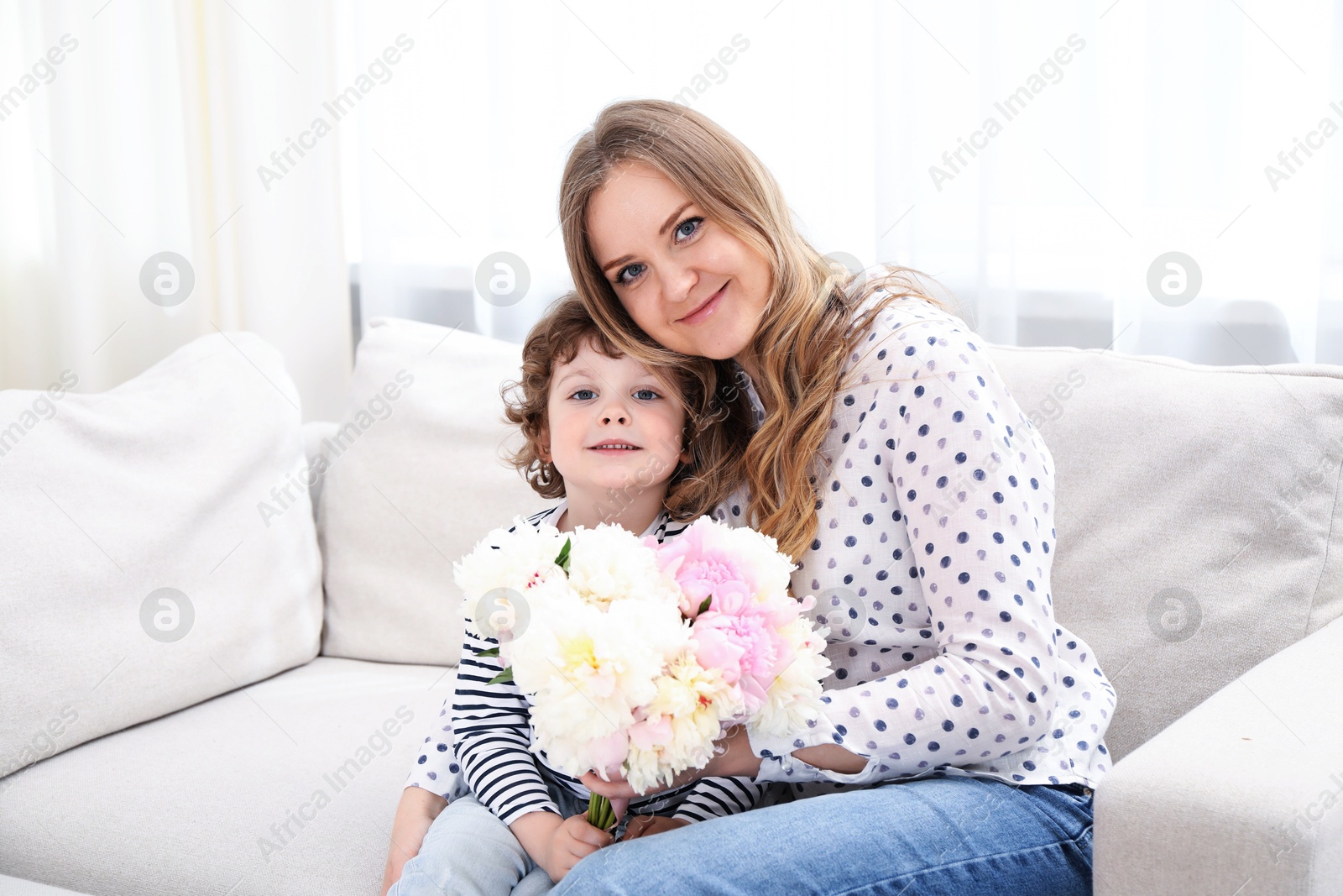 Little boy giving his mom beautiful peony flowers on sofa at home. Space for text Photo of Little boy giving his mom beautiful peony flowers on sofa at home. Space for text