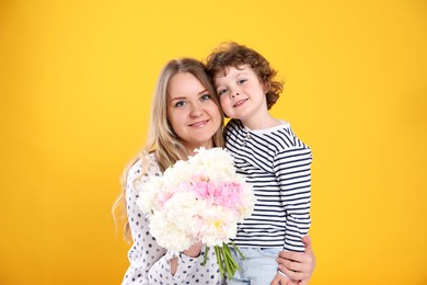 Photo of Little boy giving his mom beautiful peony flowers on yellow background