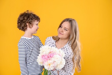Photo of Little boy giving his mom beautiful peony flowers on yellow background