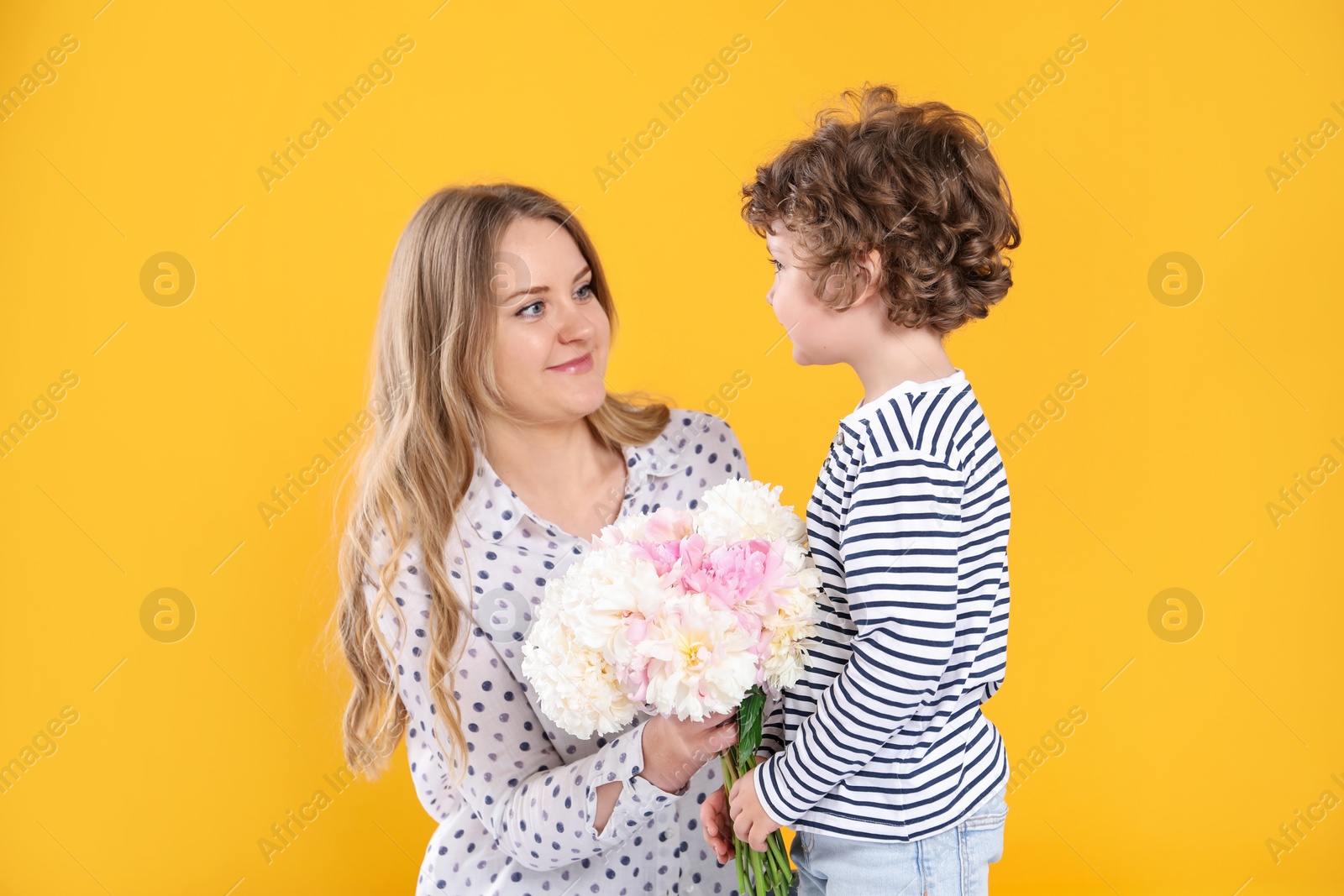 Little boy giving his mom beautiful peony flowers on yellow background Photo of Little boy giving his mom beautiful peony flowers on yellow background