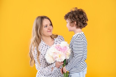 Photo of Little boy giving his mom beautiful peony flowers on yellow background