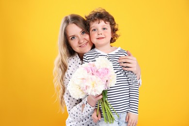 Photo of Little boy giving his mom beautiful peony flowers on yellow background